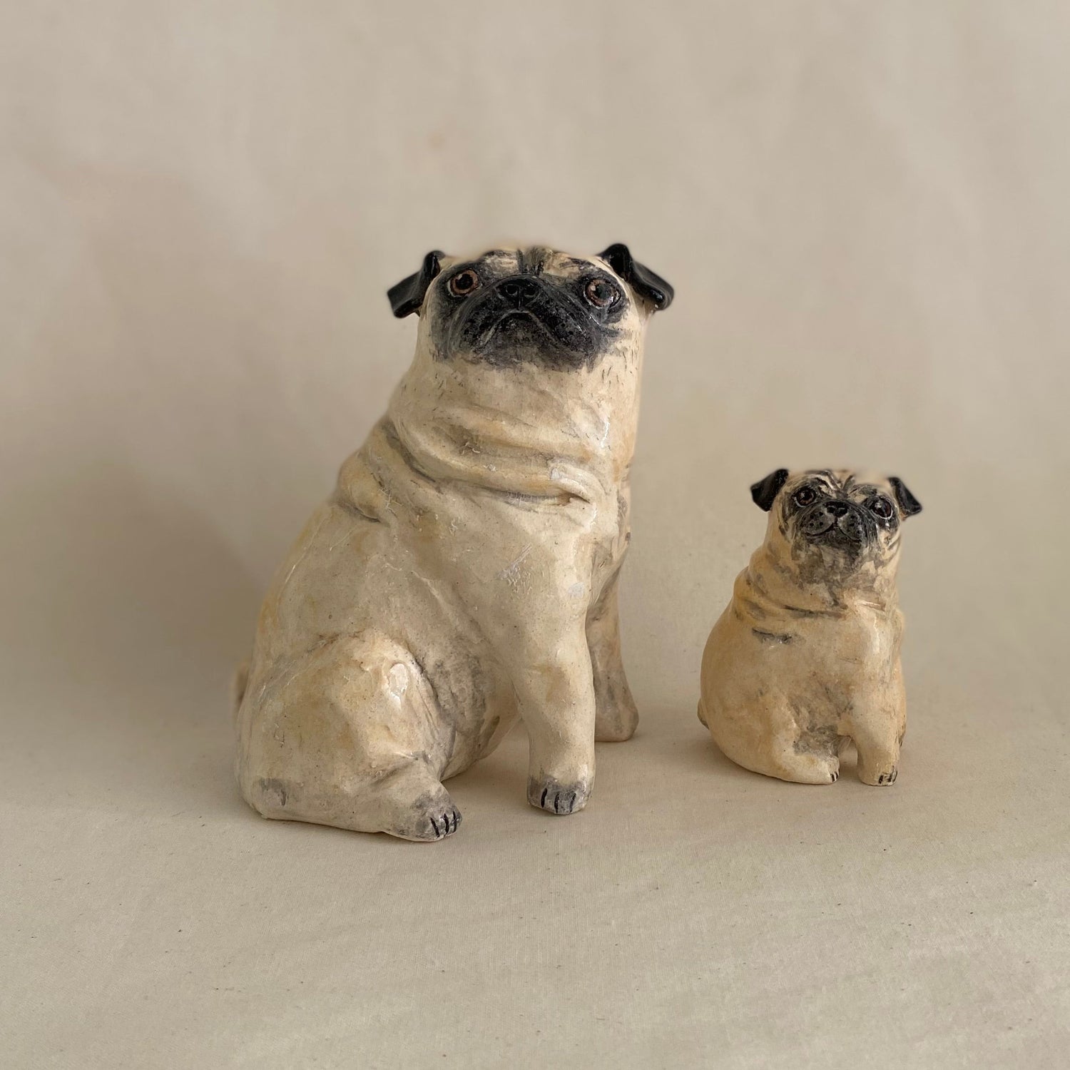 Two pug figurines on a plain background with a ruler for scale.