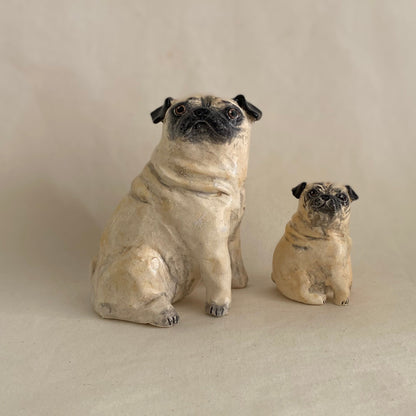 Two pug figurines on a plain background with a ruler for scale.