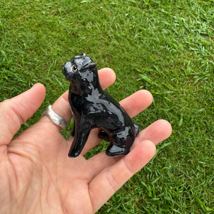 Hand holding a small black figurine against a grassy background